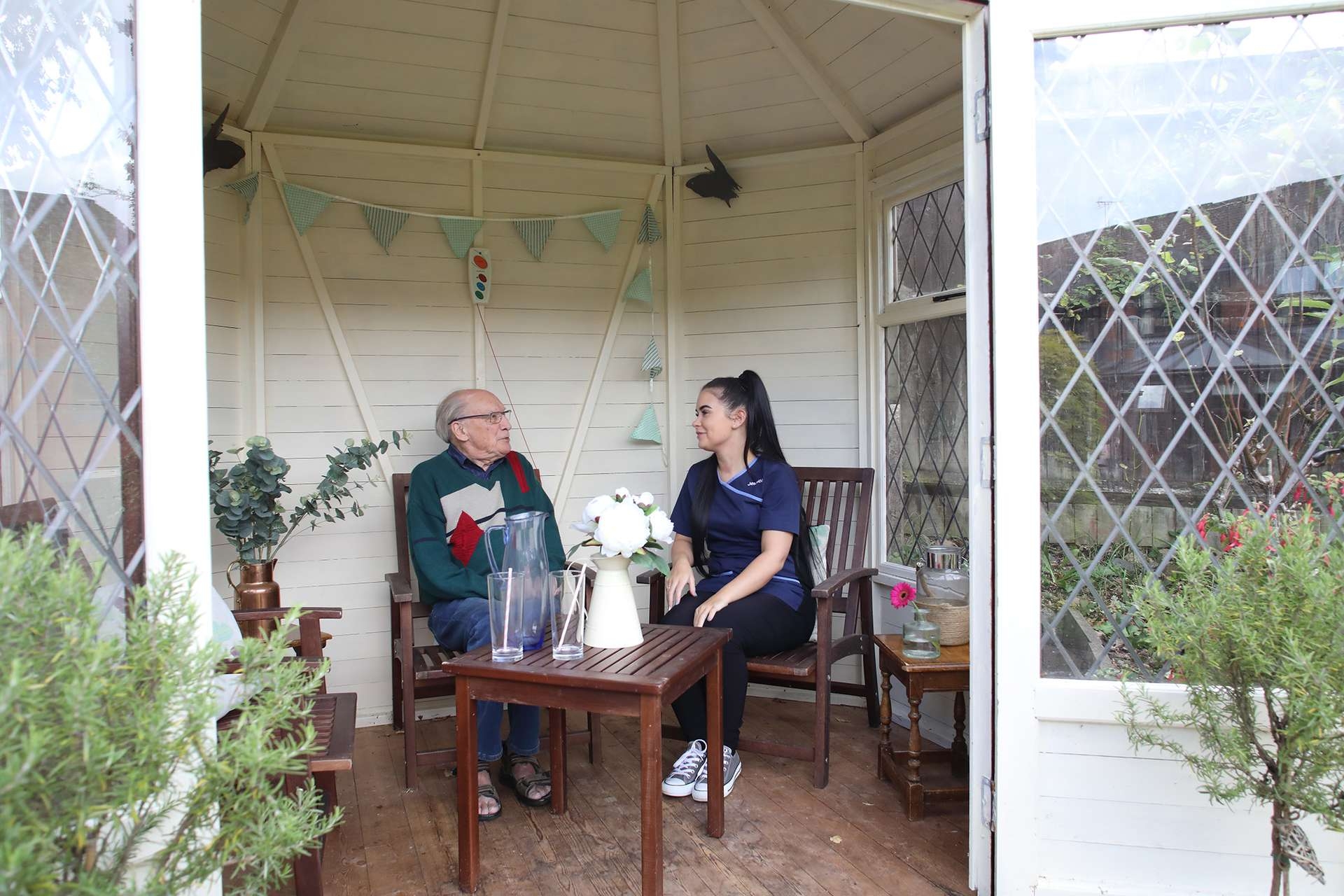 CCH Kingsleigh Gallery Image displaying a resident and carer sat at the outside table enjoying conversation
