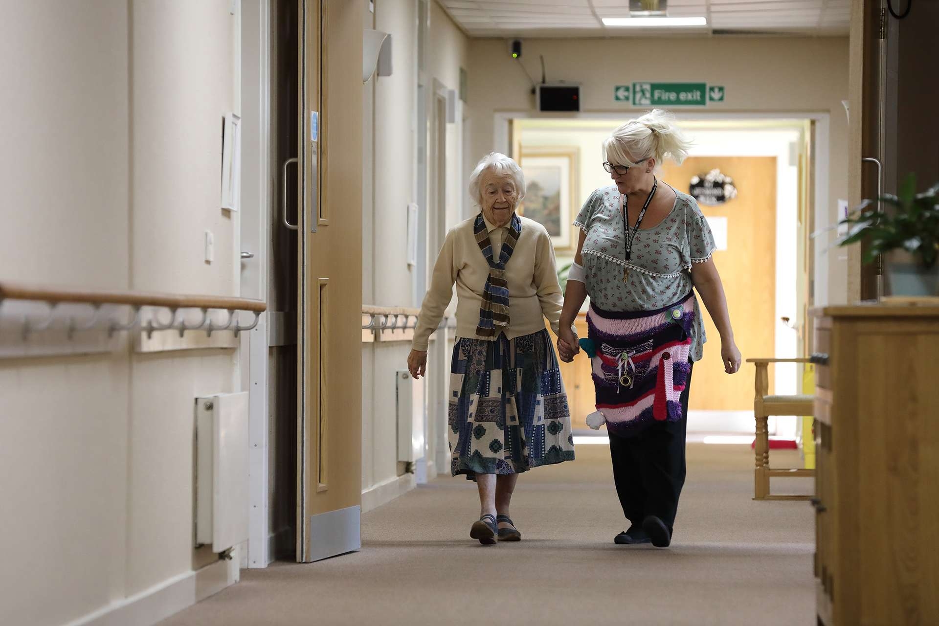 CCH Gallery Image displaying a carer holding a residents hand walking and talking